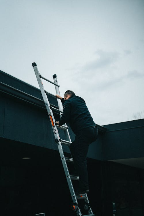 A commercial roofing contractor climbing a ladder towards the roof
