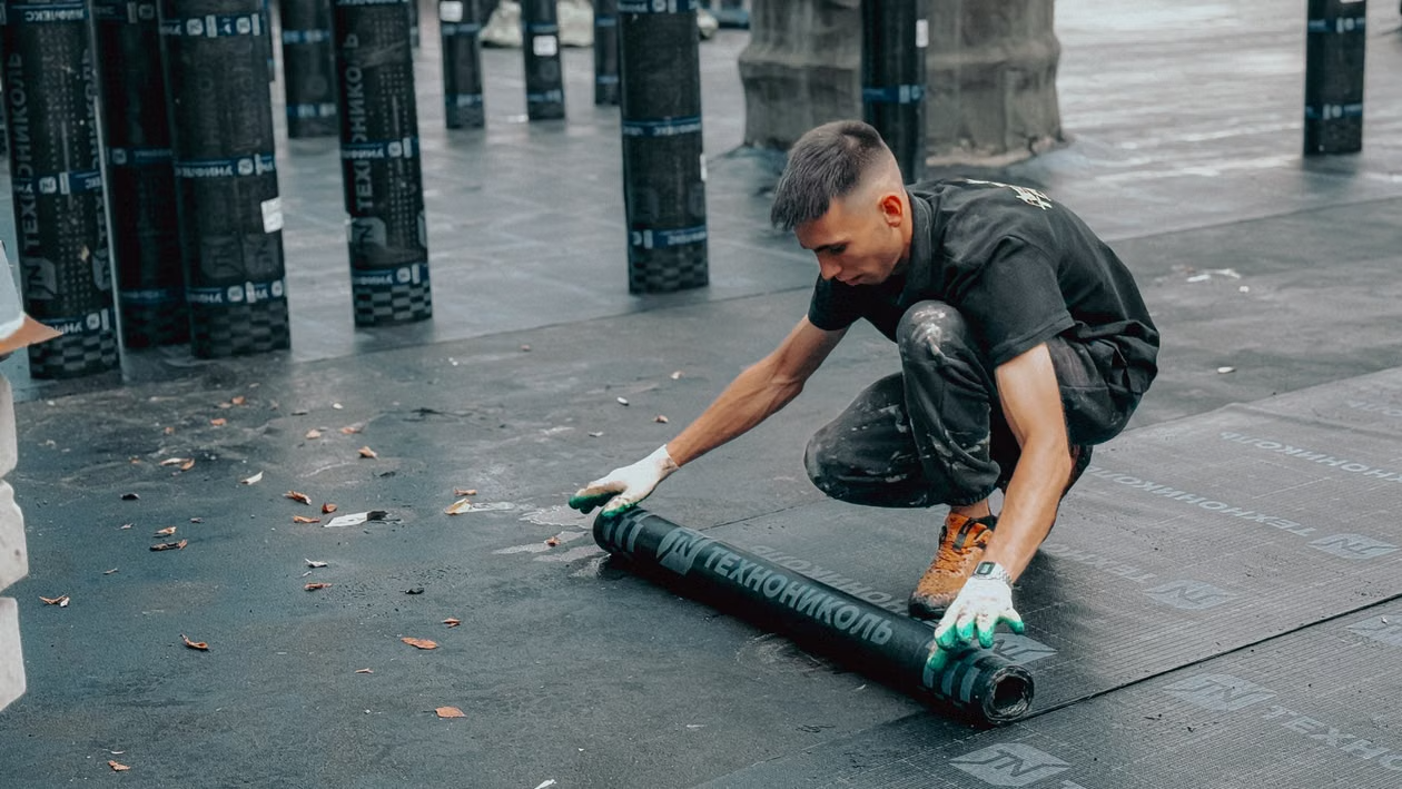 A roofer applying a waterproof membrane to a flat commercial roof.