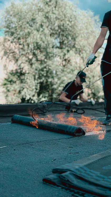 Roofers applying torch-down rubber membrane for waterproofing. 