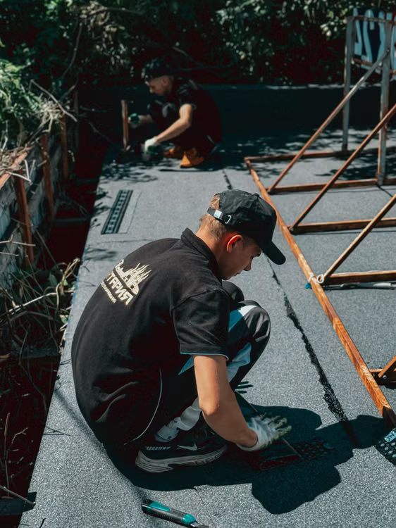 Two workers applying waterproofing membrane on a building rooftop